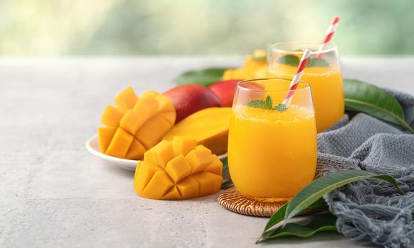 Fresh beautiful delicious mango juice. Close up design concept of smoothie cold drink in a glass cup with paper straw on gray table background.