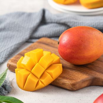 Diced fresh mango fruit on a white plate over wooden cutting board with leaves on gray table background.