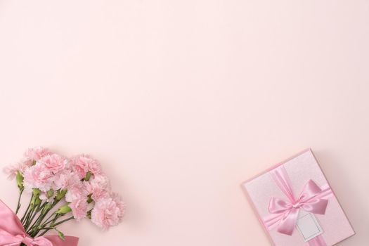 Mother's day background concept. Top view design of holiday greeting gift with carnation bouquet on bright pink table background