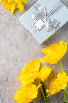 Mother's day background concept. Top view design of holiday greeting gift with yellow tulip bouquet on bright gray table background