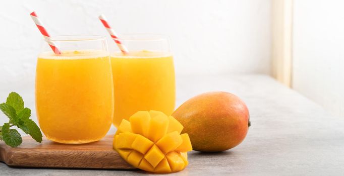 Fresh mango juice. Close up design concept of smoothie cold drink in a glass cup with paper straw on gray table background.