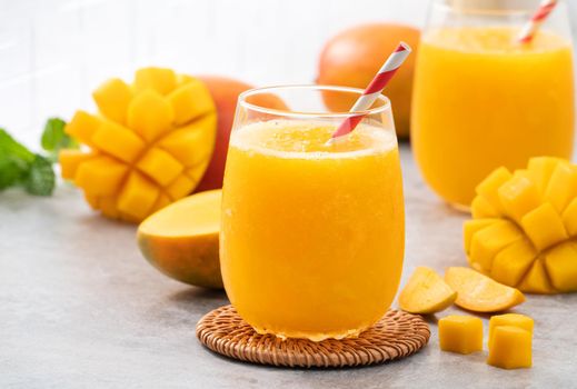 Fresh mango juice. Close up design concept of smoothie cold drink in a glass cup with paper straw on gray table background.