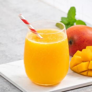 Fresh mango juice. Close up design concept of smoothie cold drink in a glass cup with paper straw on gray table background.