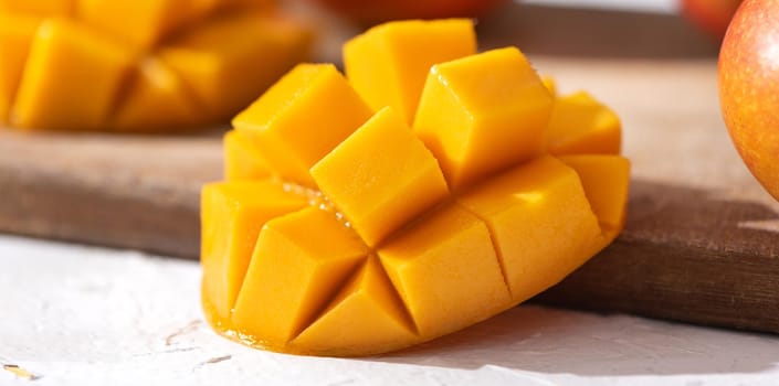 Diced fresh mango fruit on wooden cutting board with sunlight and leaf shadow at home kitchen in the afternoon.