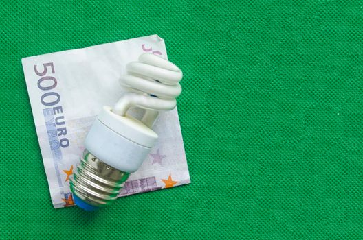 Energy-saving lamp and euro banknote on green background, copyspace.The concept of saving money in energy saving.