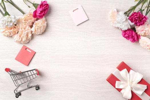 Design concept of Mother's Day greeting with carnation flower, holiday gift idea and shopping cart on wooden background.