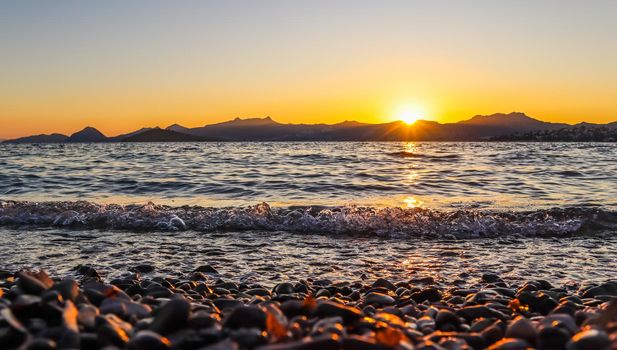 Beautiful sunset on the Mediterranean coast with islands and mountains. Stones on the beach lit by sunlight