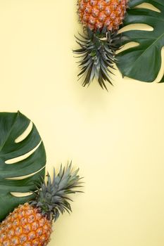Top view of fresh pineapple with tropical palm and monstera leaves on yellow table background.