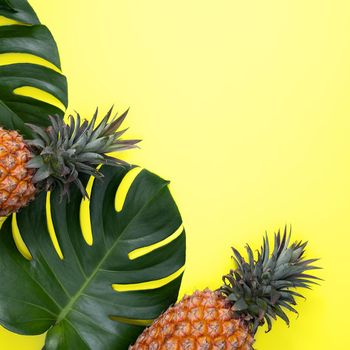 Top view of fresh pineapple with tropical palm and monstera leaves on yellow table background.
