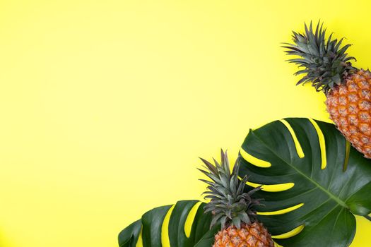 Top view of fresh pineapple with tropical palm and monstera leaves on yellow table background.