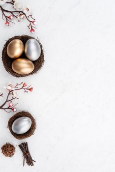 Design concept of Golden and silver Easter eggs in the nest with white plum flower on bright marble white table background.