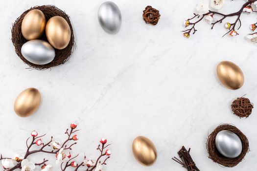 Design concept of Golden and silver Easter eggs in the nest with white plum flower on bright marble white table background.