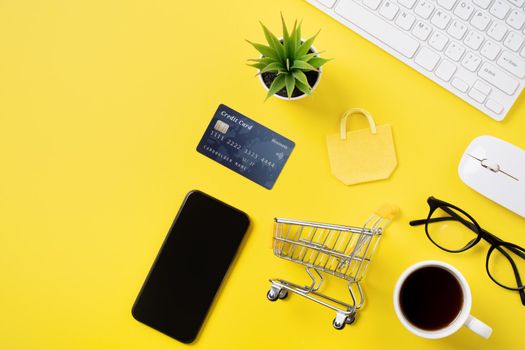 Top view of online shopping concept with credit card, smart phone and computer isolated on office yellow table background.