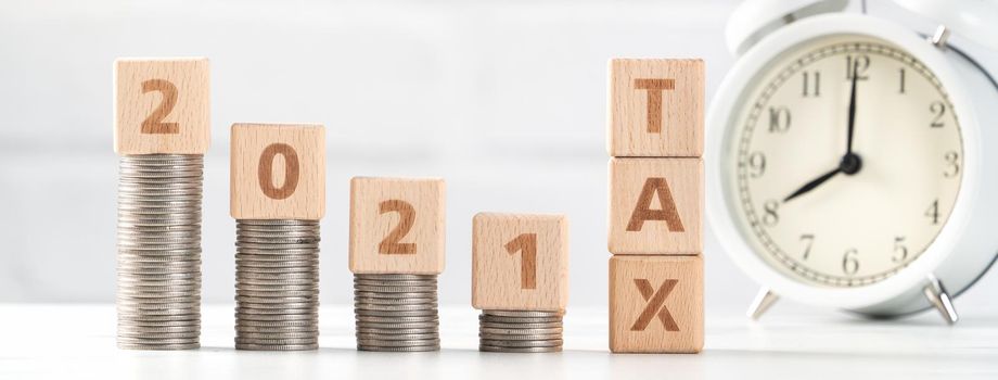 Concept of tax season approaching with wooden blocks, coins and alarm clock over white background.