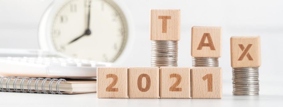 Concept of tax season approaching with wooden blocks, coins and alarm clock over white background.