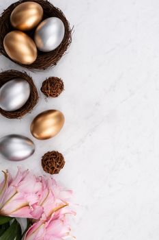 Design concept of Golden and silver Easter eggs in the nest with pink lily flower on bright marble white table background.