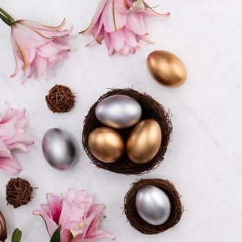 Design concept of Golden and silver Easter eggs in the nest with pink lily flower on bright marble white table background.