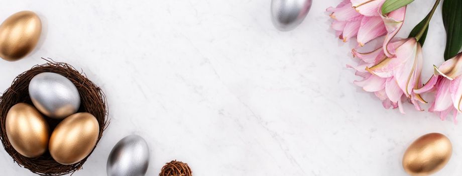Design concept of Golden and silver Easter eggs in the nest with pink lily flower on bright marble white table background.