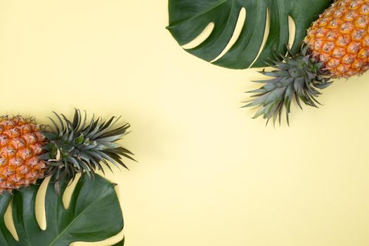 Top view of fresh pineapple with tropical palm and monstera leaves on yellow table background.