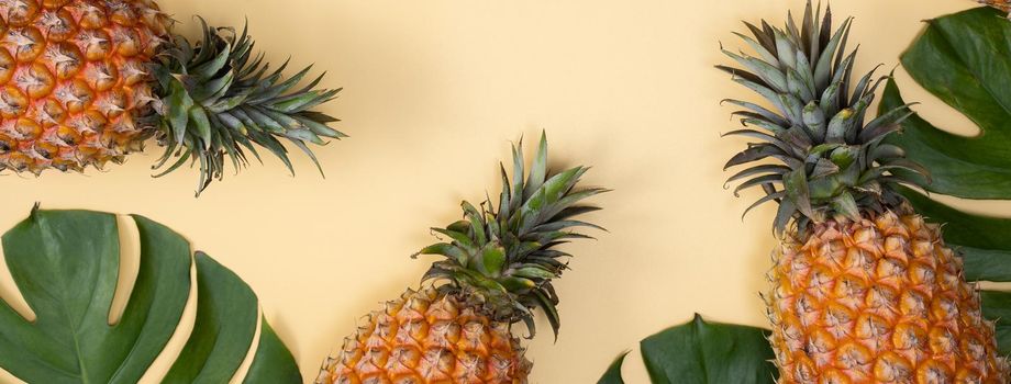 Top view of fresh pineapple with tropical palm and monstera leaves on yellow table background.