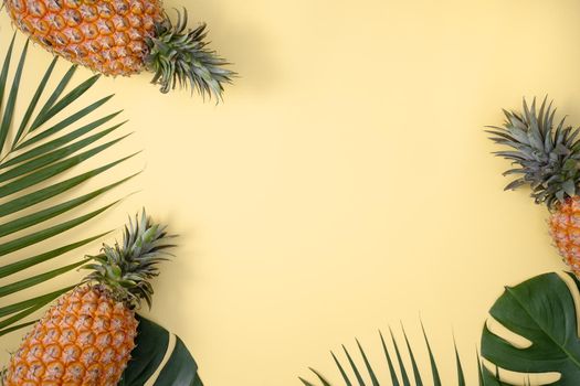 Top view of fresh pineapple with tropical palm and monstera leaves on yellow table background.