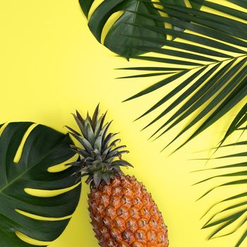 Top view of fresh pineapple with tropical palm and monstera leaves on yellow table background.