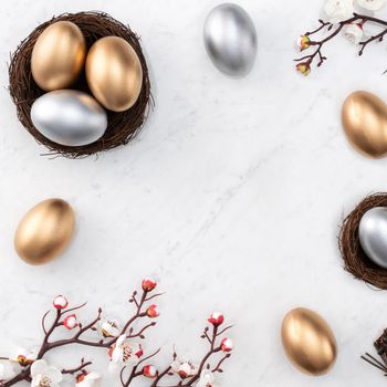 Design concept of Golden and silver Easter eggs in the nest with white plum flower on bright marble white table background.