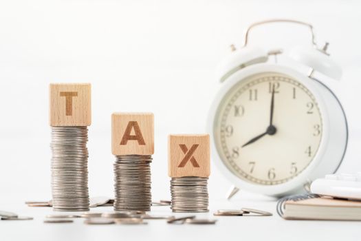 Concept of tax season approaching with wooden blocks, coins and alarm clock over white background.