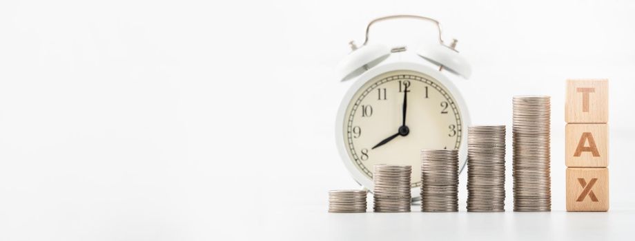 Concept of tax season approaching with wooden blocks, coins and alarm clock over white background.