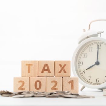 Concept of tax season approaching with wooden blocks, coins and alarm clock over white background.
