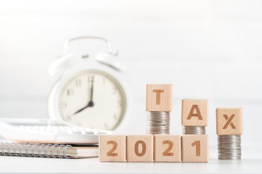 Concept of tax season approaching with wooden blocks, coins and alarm clock over white background.