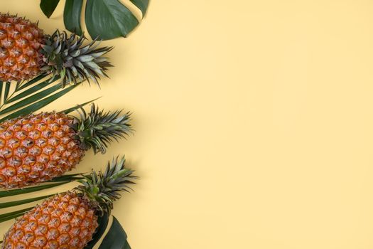 Top view of fresh pineapple with tropical palm and monstera leaves on yellow table background.