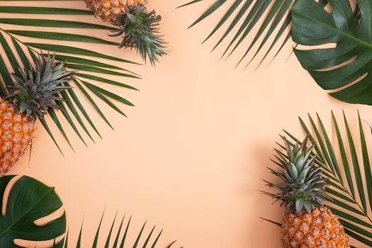 Top view of fresh pineapple with tropical palm and monstera leaves on pastel orange table background.