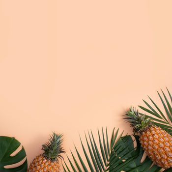 Top view of fresh pineapple with tropical palm and monstera leaves on pastel orange table background.