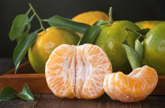 Fresh green tangerine mandarin orange with fresh leaves on dark wooden table background harvest concept.