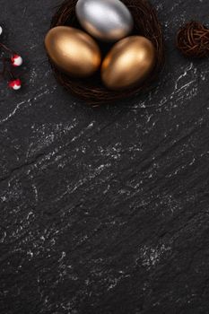 Golden and silver Easter eggs with plum blossom flower on dark black slate table background.