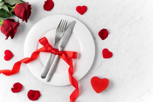 White plate with red rose flower on marble white table background for Valentine's Day dating holiday meal concept.