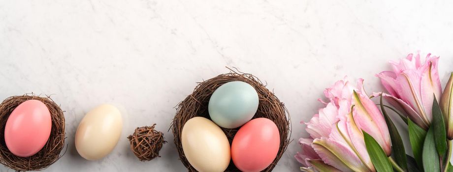 Colorful Easter eggs in the nest with pink lily flower on bright marble white table background.