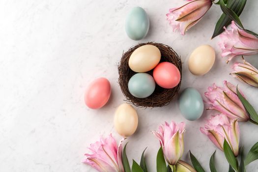 Colorful Easter eggs in the nest with pink lily flower on bright marble white table background.
