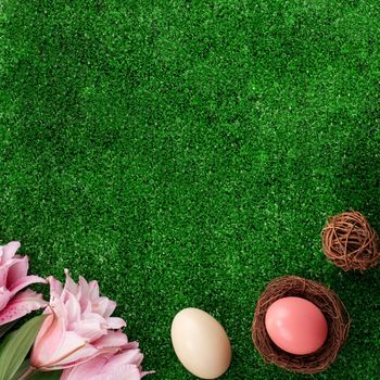 Colorful Easter eggs in the nest with pink lily flower on on a lawn grass background.