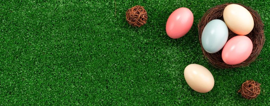 Colorful Easter eggs in the nest with pink lily flower on on a lawn grass background.