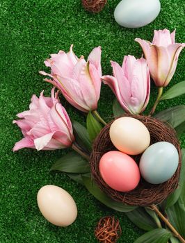Colorful Easter eggs in the nest with pink lily flower on on a lawn grass background.