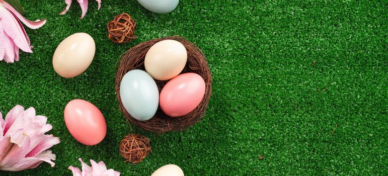 Colorful Easter eggs in the nest with pink lily flower on on a lawn grass background.