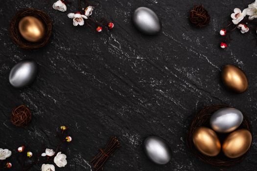 Golden and silver Easter eggs with plum blossom flower on dark black slate table background.