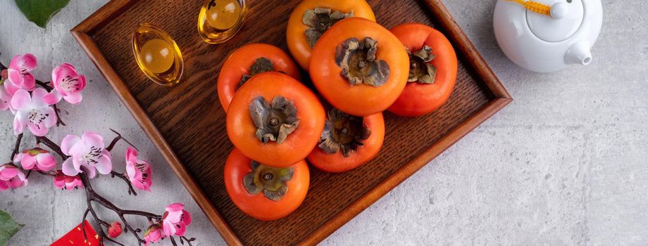 Fresh persimmons on gray table background for Chinese new year fruit design, words on the golden coin means the Dynasty name it made.
