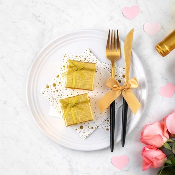 White plate with gift and pink rose flower on marble white table background for Valentine's Day special holiday dating meal concept.