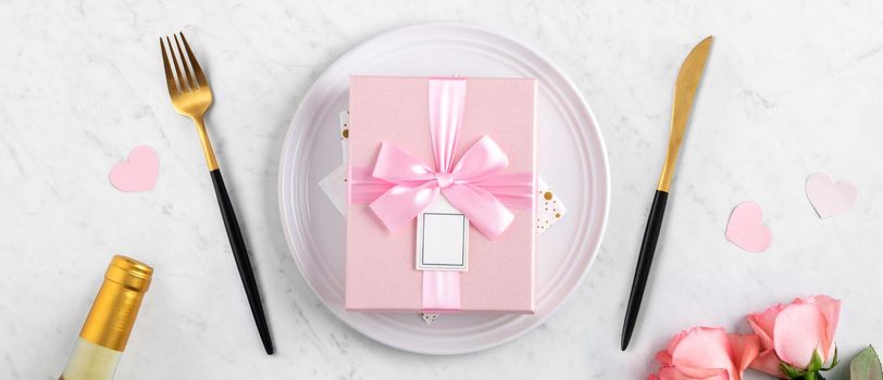 White plate with gift and pink rose flower on marble white table background for Valentine's Day special holiday dating meal concept.