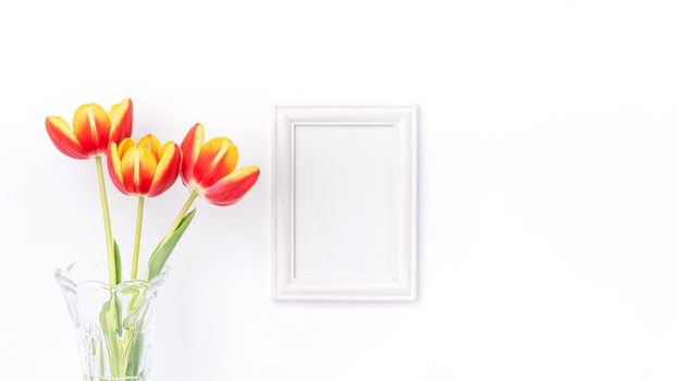 Tulip flower in glass vase with picture frame on white wall, Mother's Day decor concept.