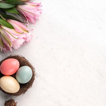 Colorful Easter eggs in the nest with pink lily flower on bright marble white table background.