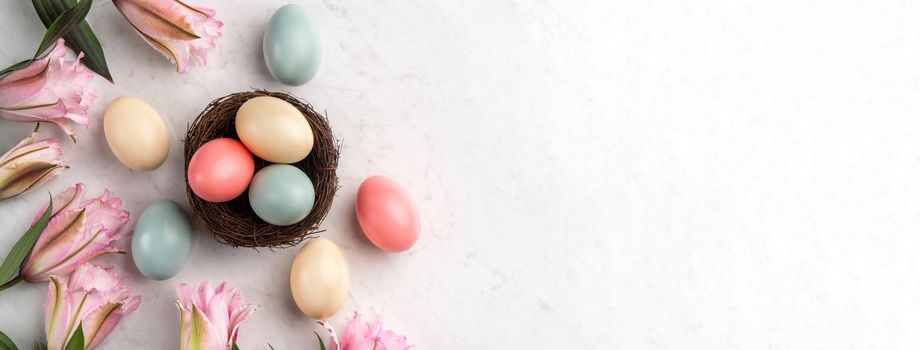 Colorful Easter eggs in the nest with pink lily flower on bright marble white table background.